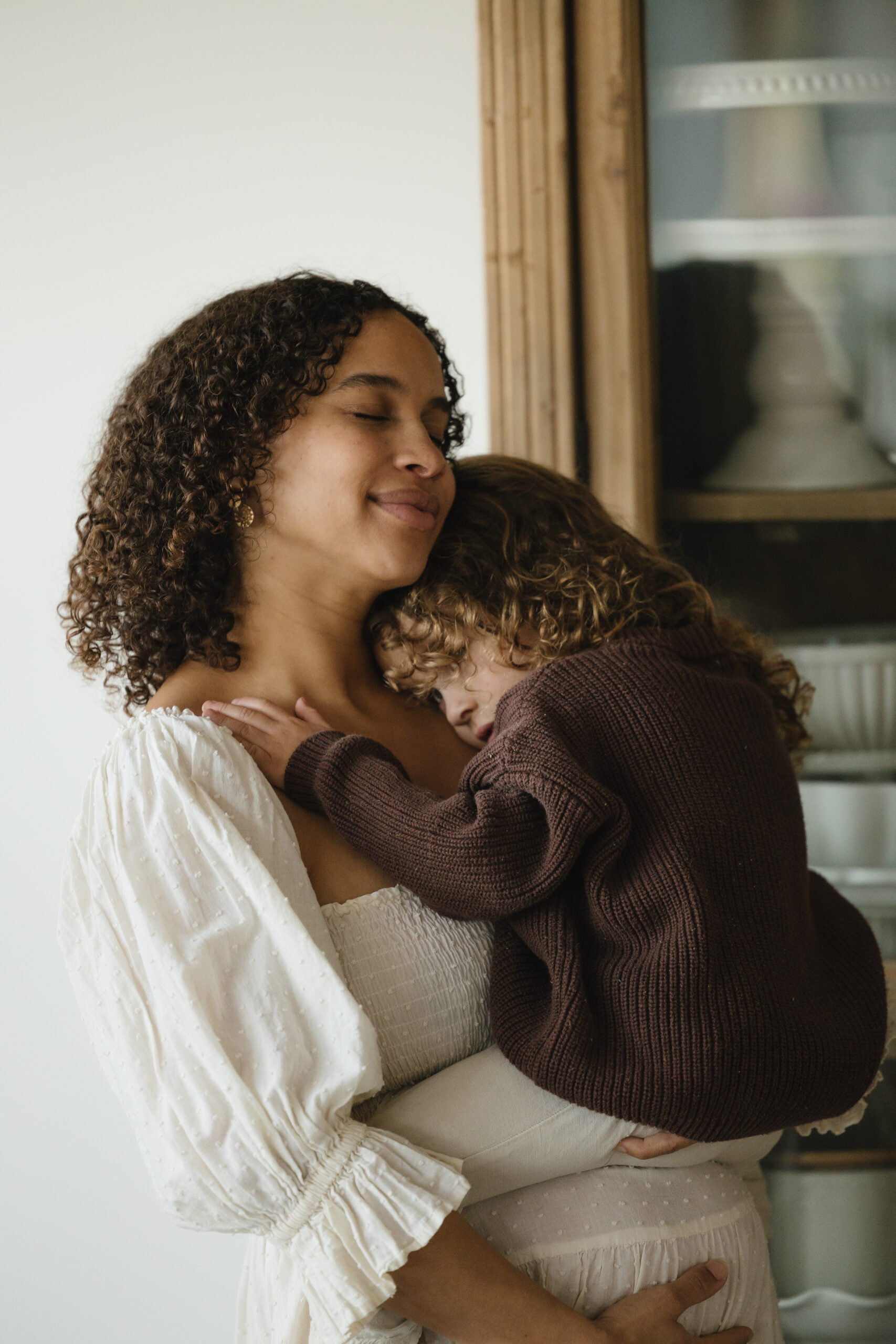 Mother holding her young child close in front of a window